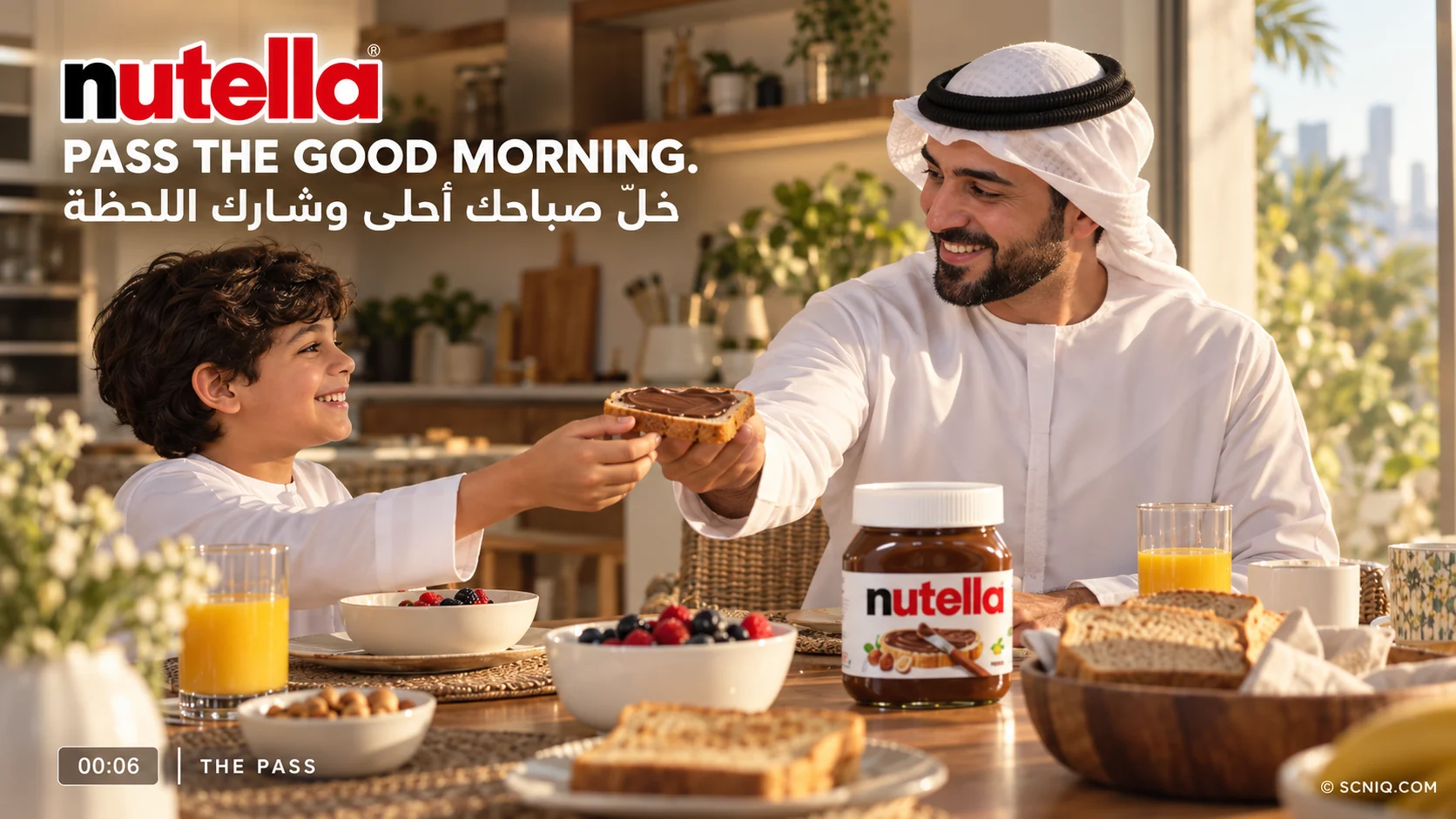A smiling son hands a slice of Nutella toast to his father across a sunlit breakfast table, the jar between them